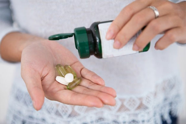 زن در حال استفاده از مولتی ویتامین - جعبه مولتی ویتامین در دست 